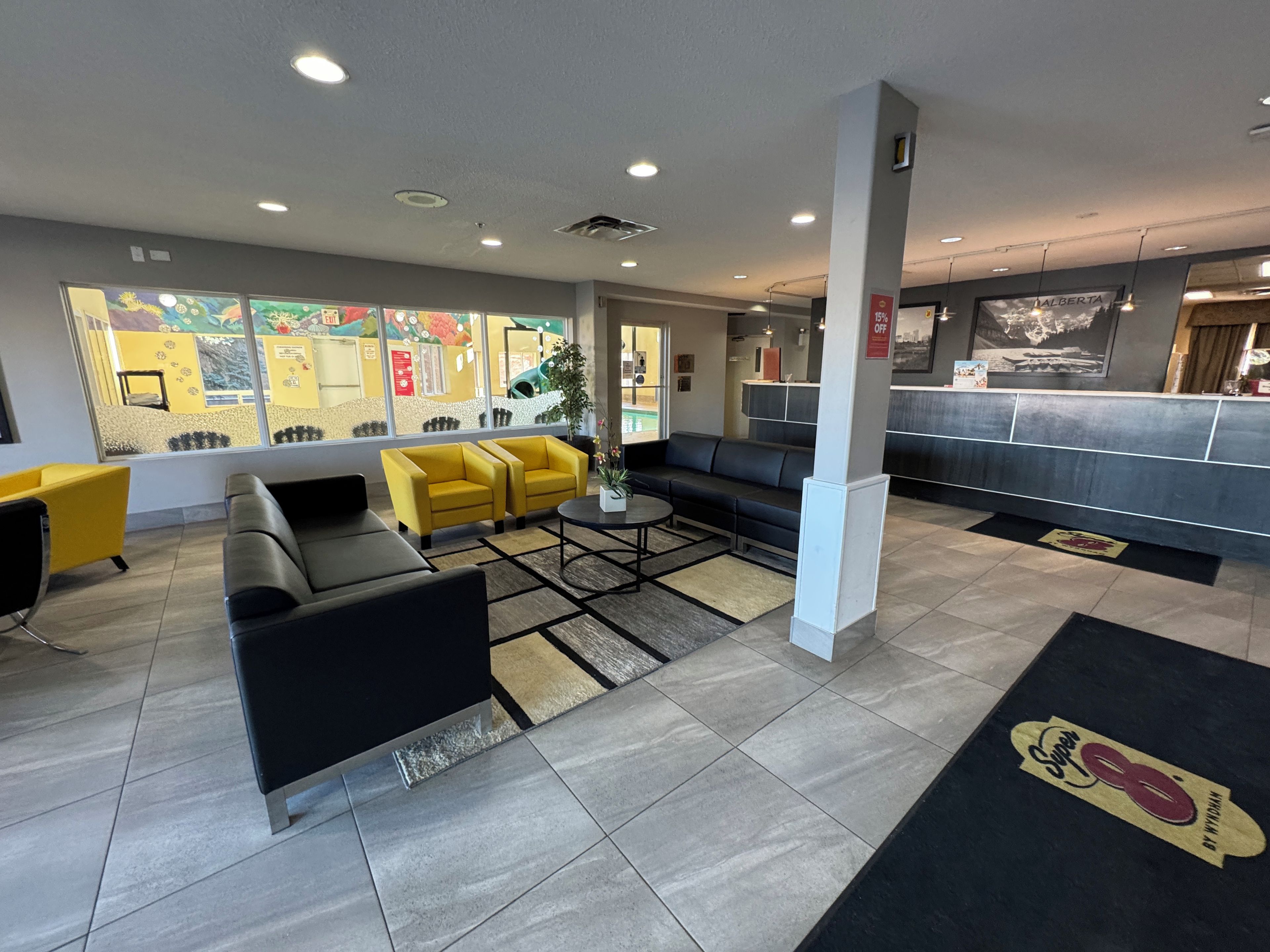 A hotel lobby with seating areas, a reception desk, and a large window with artwork.
