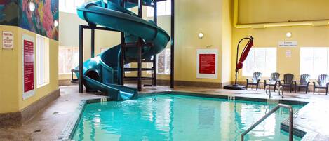 An indoor swimming pool with a blue spiral slide, safety signs, and a mural on the wall.