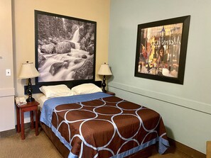 Cozy retreat with a neatly made bed, wall-mounted lamps, and a serene waterfall photograph above.