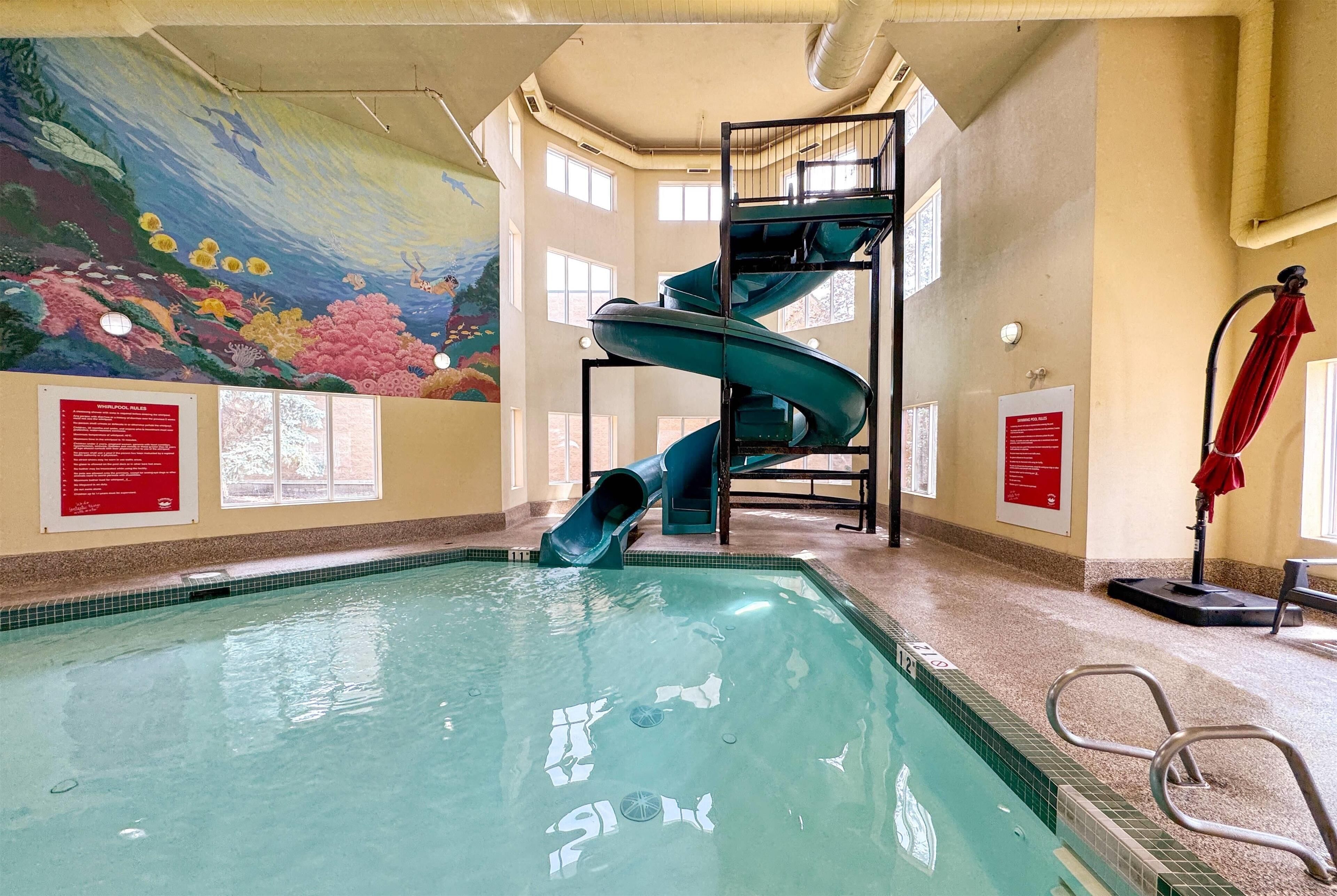 Una piscina interior con un tobogán en espiral, un mural y carteles informativos.