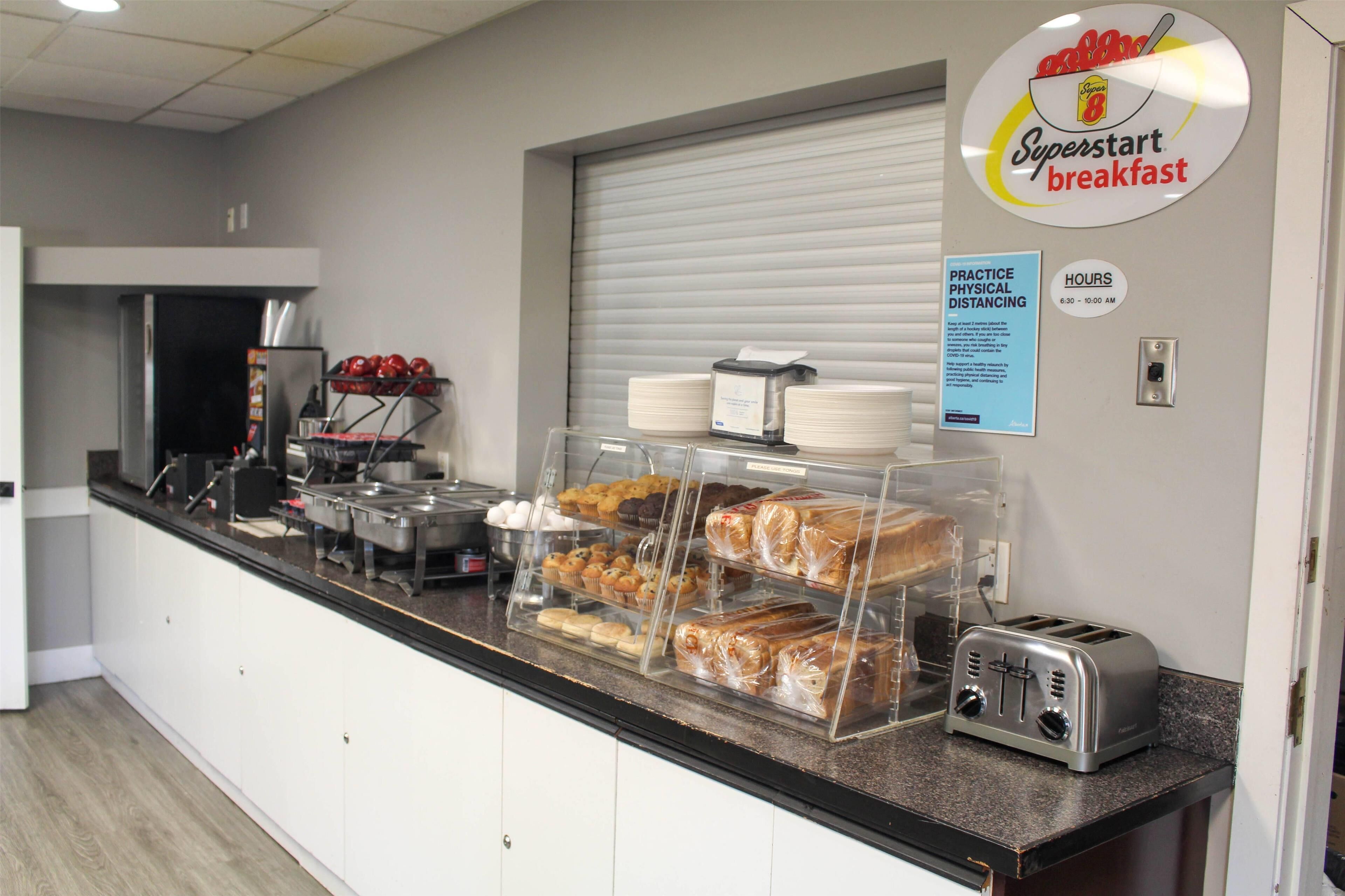 A breakfast counter with various pastries and bread, a toaster, and a sign indicating hours of operation.