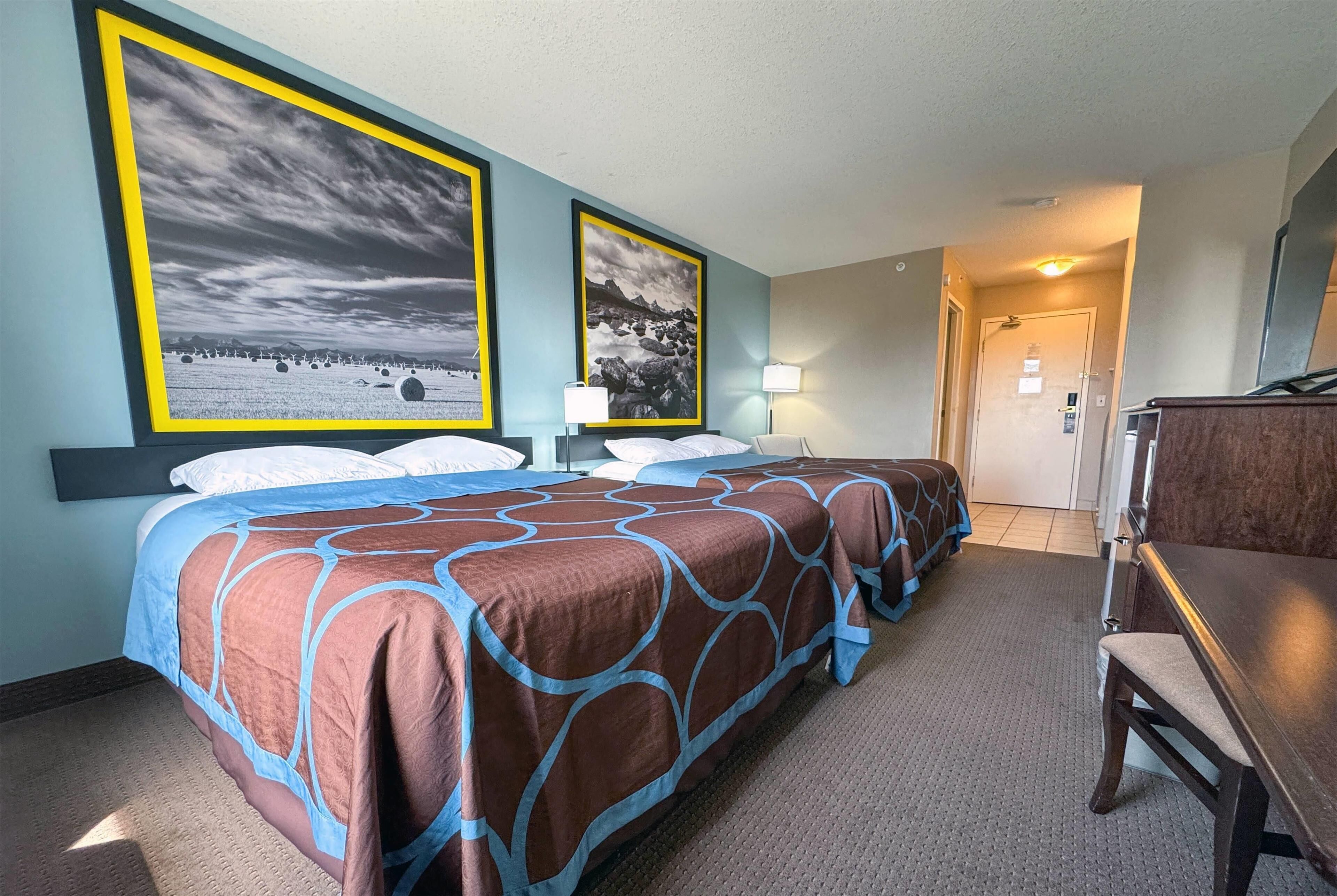 A hotel room with a large bed, two framed pictures on the wall, a desk, and a chair.
