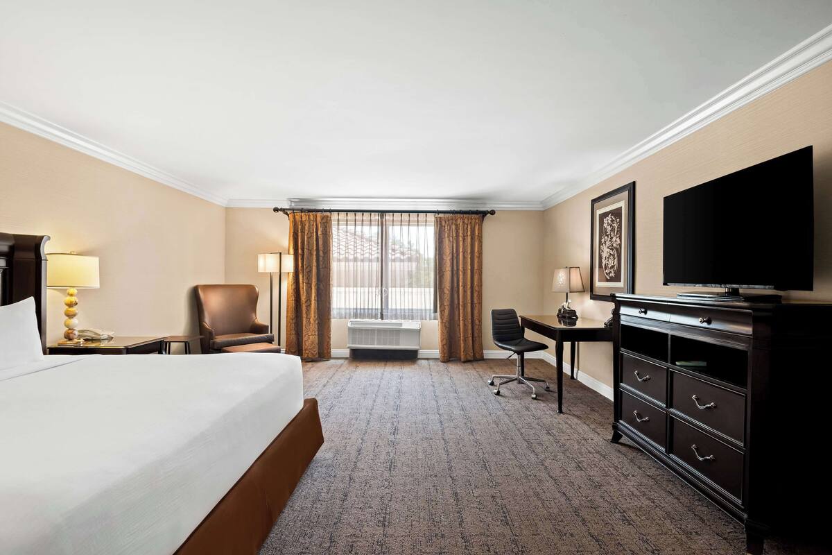 A hotel room with a large bed, a desk with a chair, a television, and a dresser.