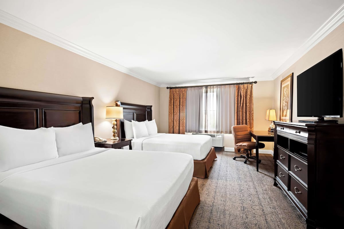 A hotel room with two beds, a desk, a chair, a television, and a dresser.