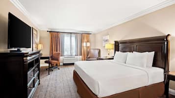A hotel room with a large bed, a flat-screen TV, a desk with a lamp, a chair, and a window with curtains.