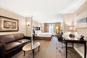 Classic design with a large bed, sofa, and desk, set against a backdrop of framed artworks and a chandelier.