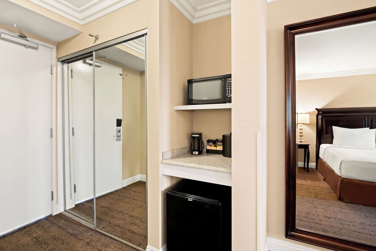 A hotel room with a bed, a microwave, a coffee maker, and a mini fridge.