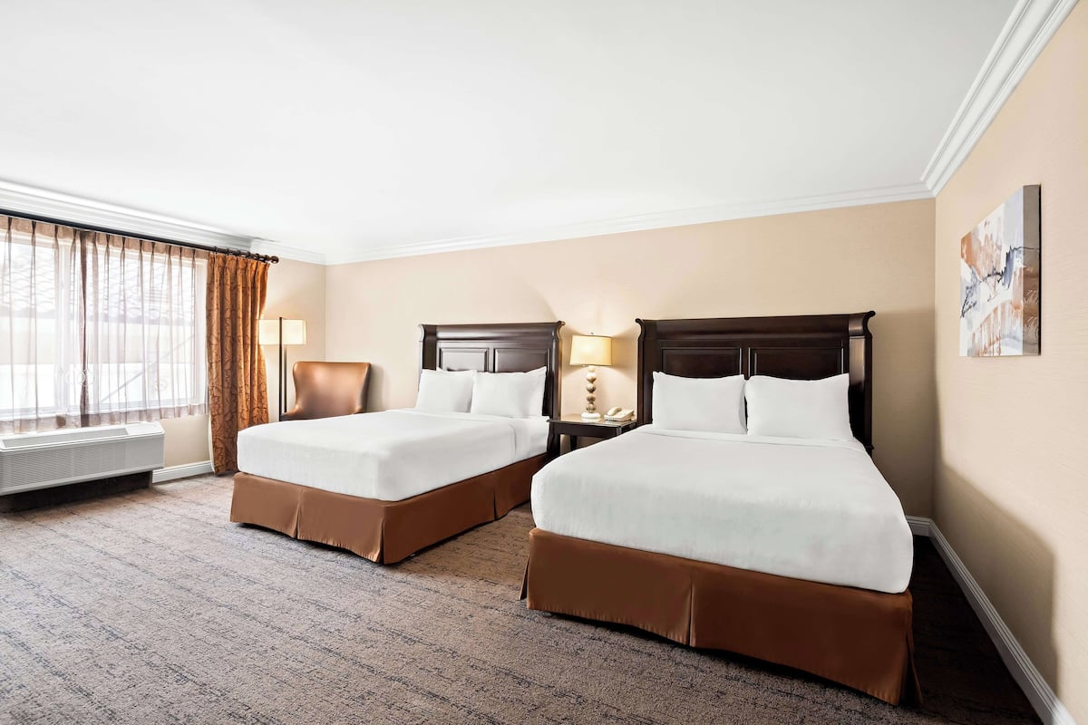 A hotel room with two beds, a desk, a chair, a lamp, and a painting on the wall.