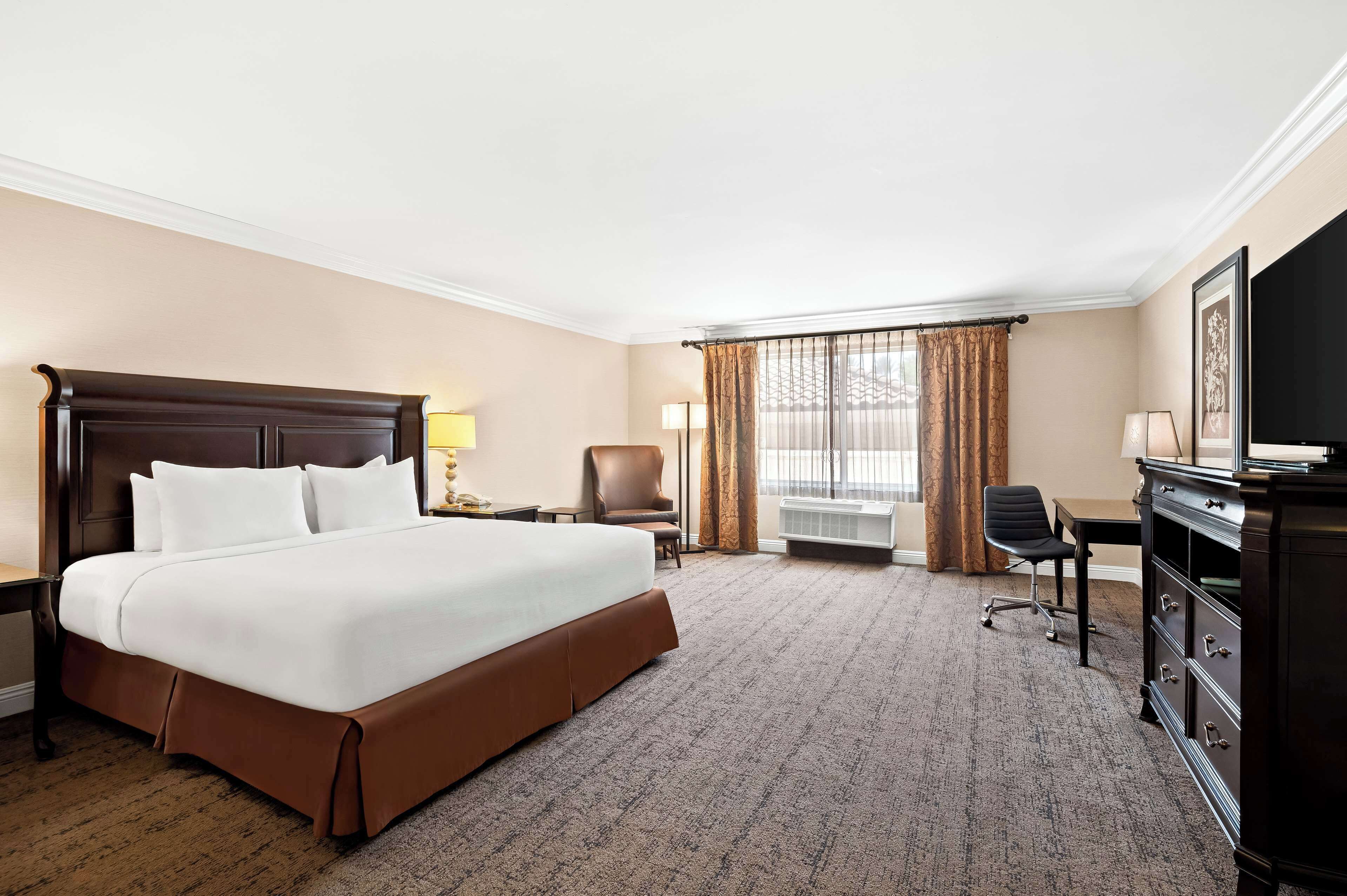 A hotel room with a large bed, a desk, a chair, a dresser, and a television.