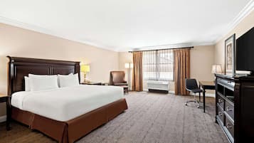 A hotel room with a large bed, a desk, a chair, a dresser, and a television.