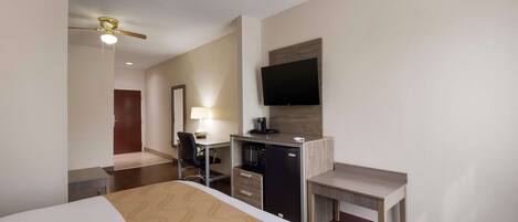 A hotel room with a bed, desk, chair, and a television on the wall.