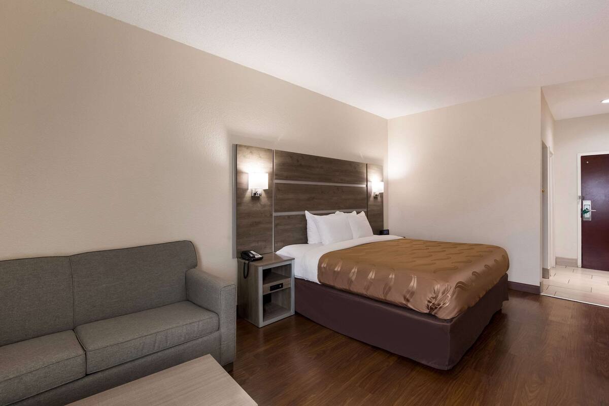 Ein Hotelzimmer mit einem Bett, einem Nachttisch mit Lampe, einer Couch und einem Holzboden.