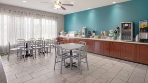 A modern kitchen with a teal accent wall, a dining area with metal chairs and a table, and a coffee machine.