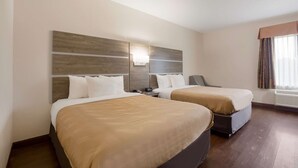 A hotel room with two beds, a nightstand, a lamp, and a window with curtains.