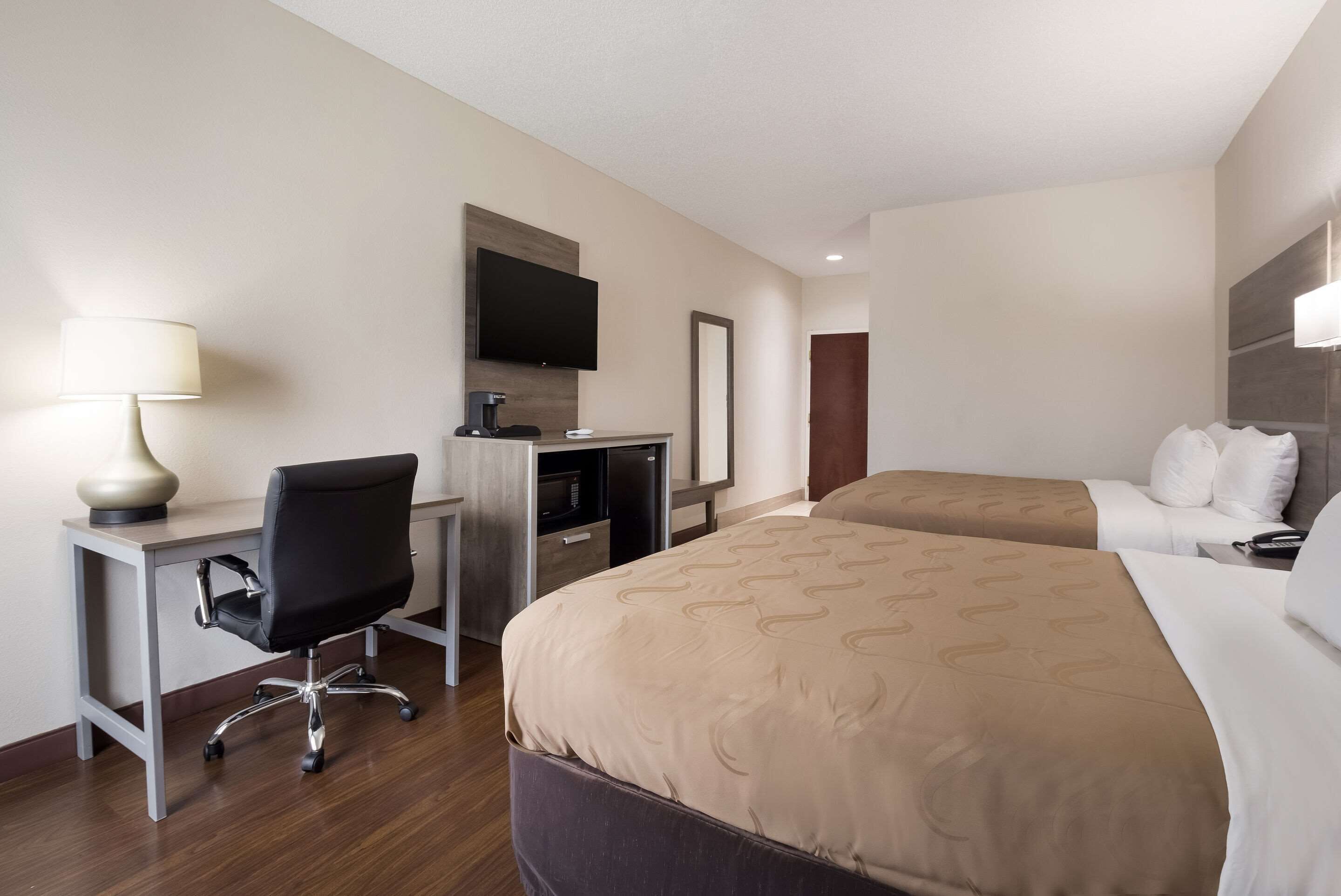 A hotel room with a desk, two beds, a TV, and a mirror.