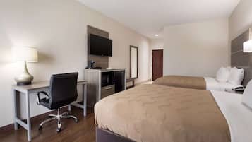 A hotel room with a desk, two beds, a TV, and a mirror.