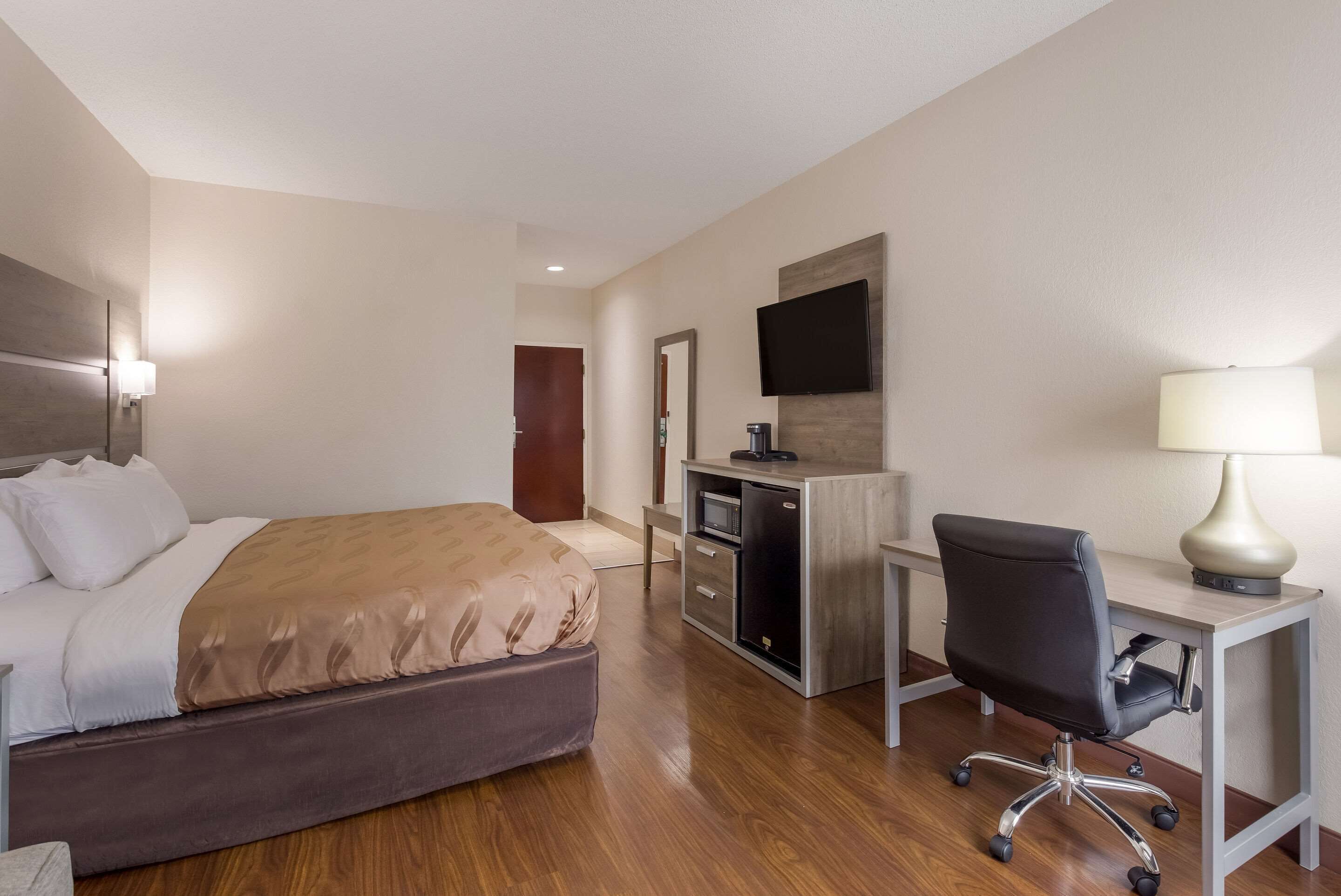 Una habitación de hotel con cama, escritorio, silla, televisión y una pequeña cocina.