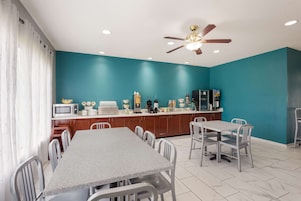 Una cocina moderna con paredes azul verdosas, un comedor con mesa de granito y un ventilador de techo.