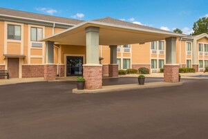 Una entrada de hotel con un vestíbulo cubierto, pilares de ladrillo y plantas en macetas.