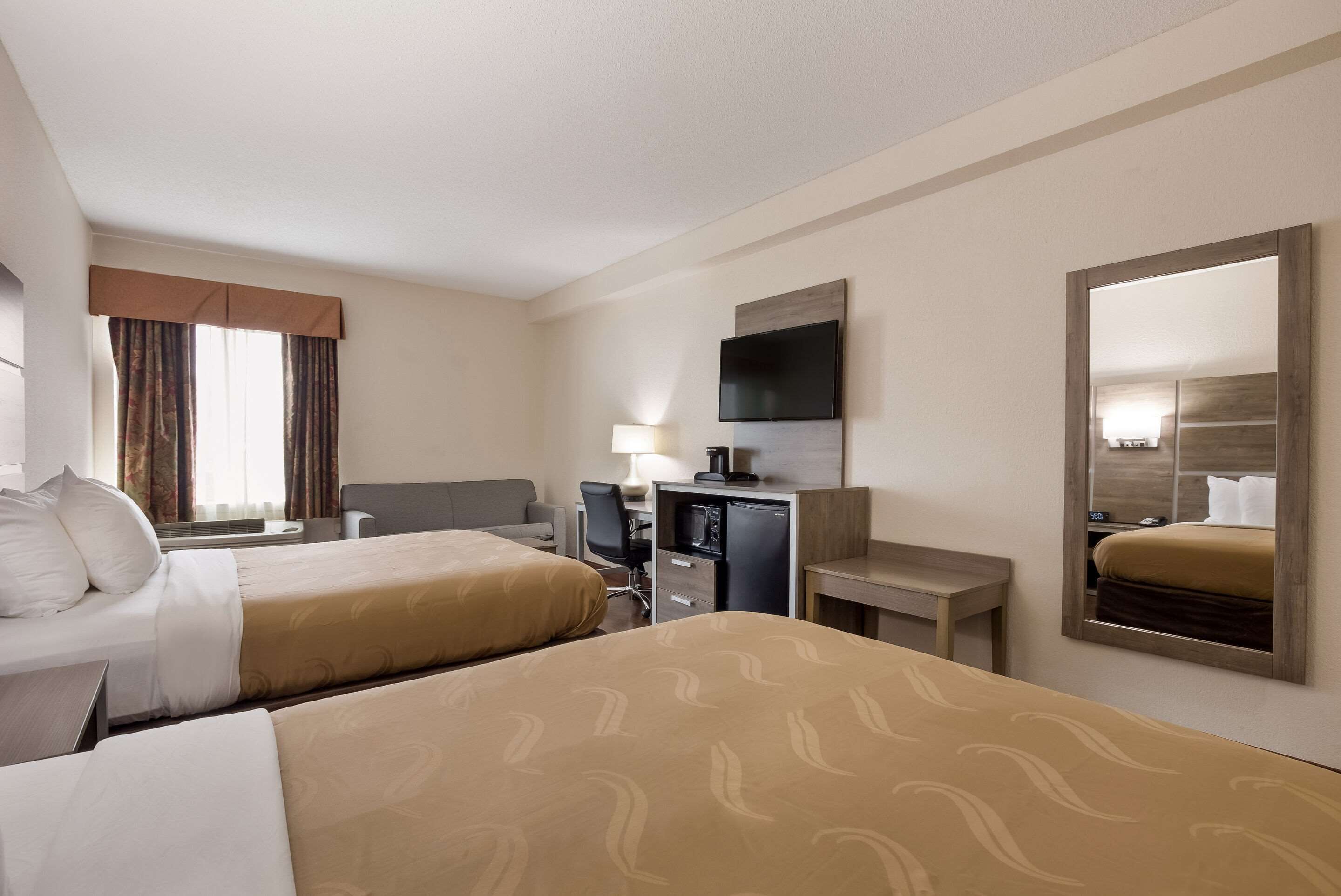 A hotel room with two beds, a desk, a television, and a mirror.
