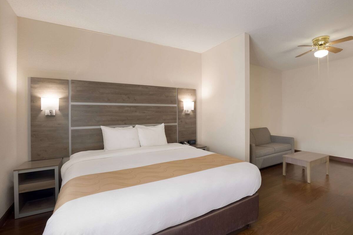 Ein Hotelzimmer mit einem großen Bett, einem Nachttisch, einer Couch, einem kleinen Tisch und einem Deckenventilator.