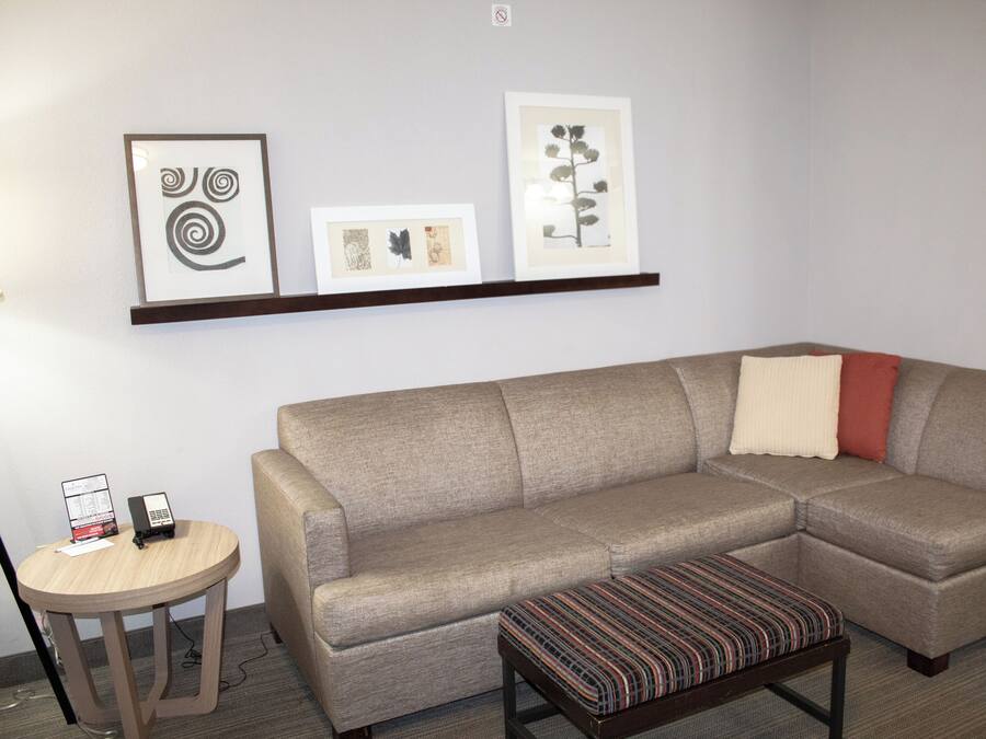 Un salon avec un canapé d’angle beige, une petite table ronde sur laquelle se trouve un téléphone, et une collection d’œuvres d’art encadrées accrochées au mur.