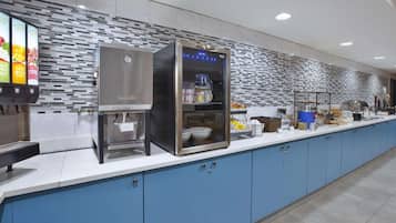 Un área de cocina moderna con una cafetera, un enfriador refrigerado y un mostrador de exhibición de alimentos.