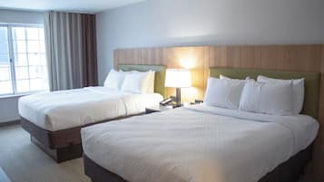 A hotel room with two beds, a wooden headboard, a bedside lamp, and a window with curtains.