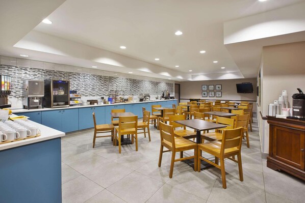 A modern restaurant with blue cabinets, wooden tables and chairs, and a kitchen area with appliances.