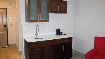 A kitchen with dark wooden cabinets, a white countertop, and a red chair.
