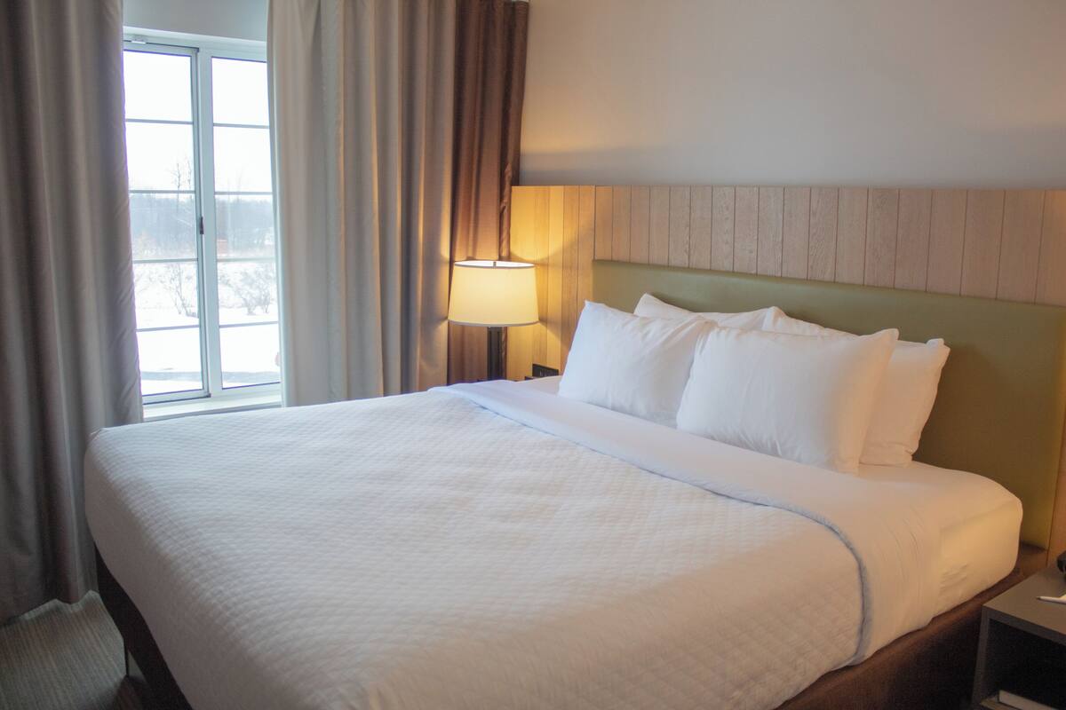 A hotel room with a large bed, a nightstand with a lamp, and a window with curtains.