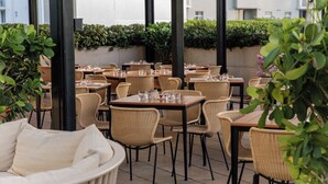 An outdoor dining area with wicker furniture and tables, surrounded by greenery and with a view of a building in the background. - Four Seasons Hotel Miami (Miami)