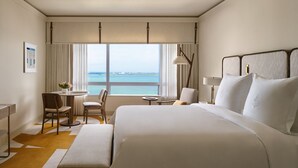 Une chambre d’hôtel avec un grand lit, un bureau, une chaise, une petite table et une vue sur la mer.