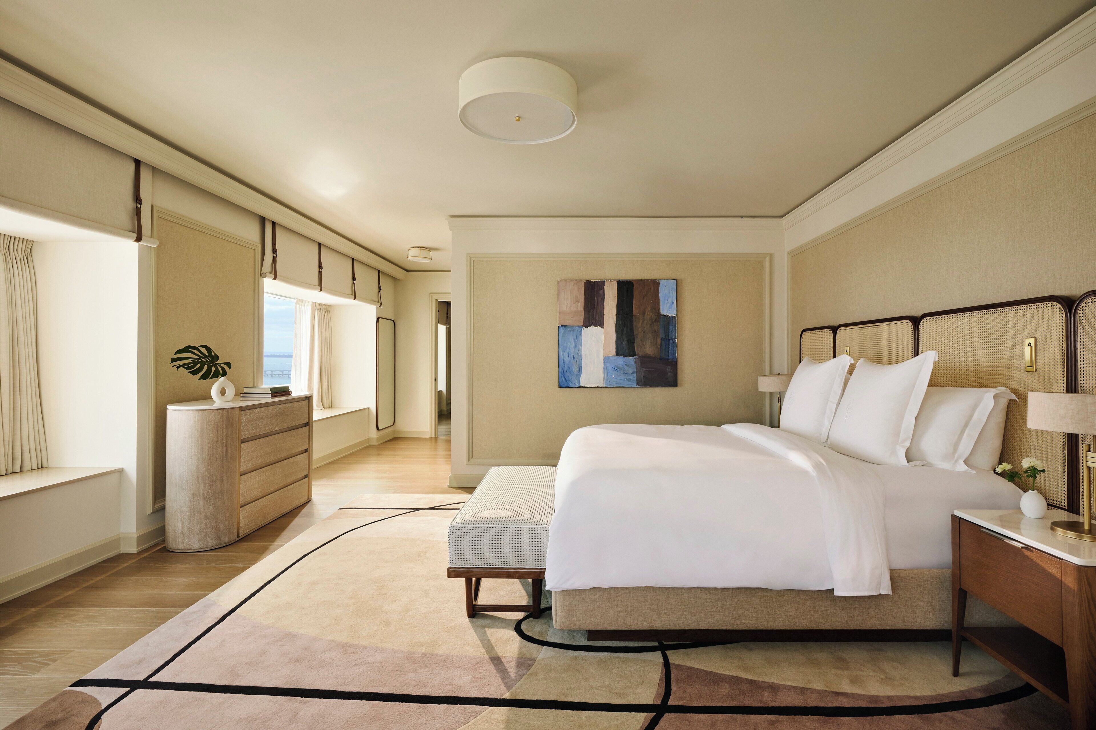 A modern bedroom with a large bed, a bedside table, a dresser, and a window with curtains.