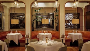 Un restaurant avec des banquettes et des tables rondes, chacune étant recouverte d’une nappe blanche et agrémentée de couverts en argent.