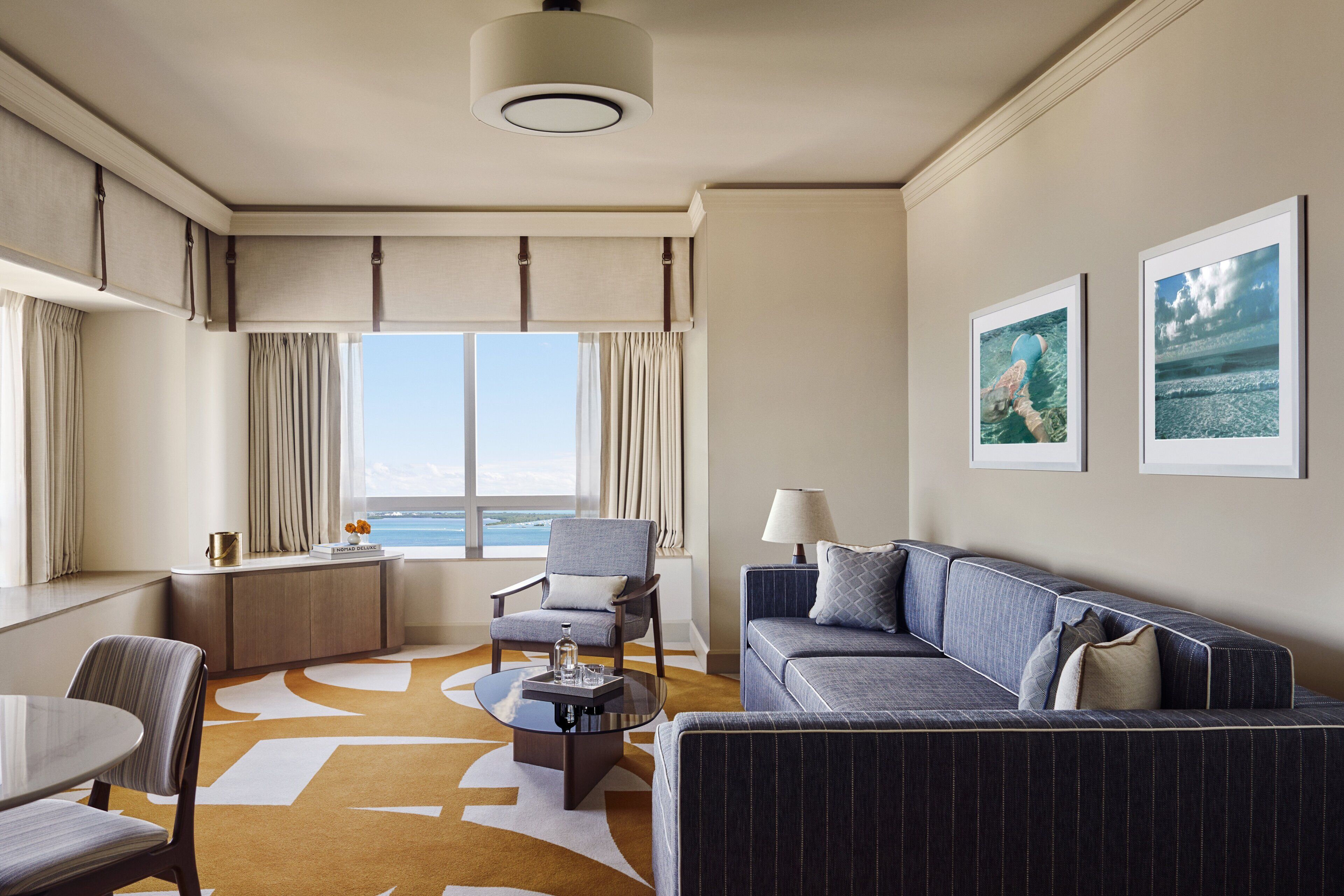 Habitación de hotel con un ventanal grande, un sofá, una silla, una mesita y un escritorio.