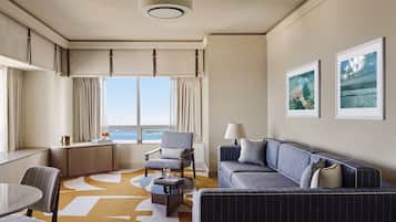 Habitación de hotel con un ventanal grande, un sofá, una silla, una mesita y un escritorio.