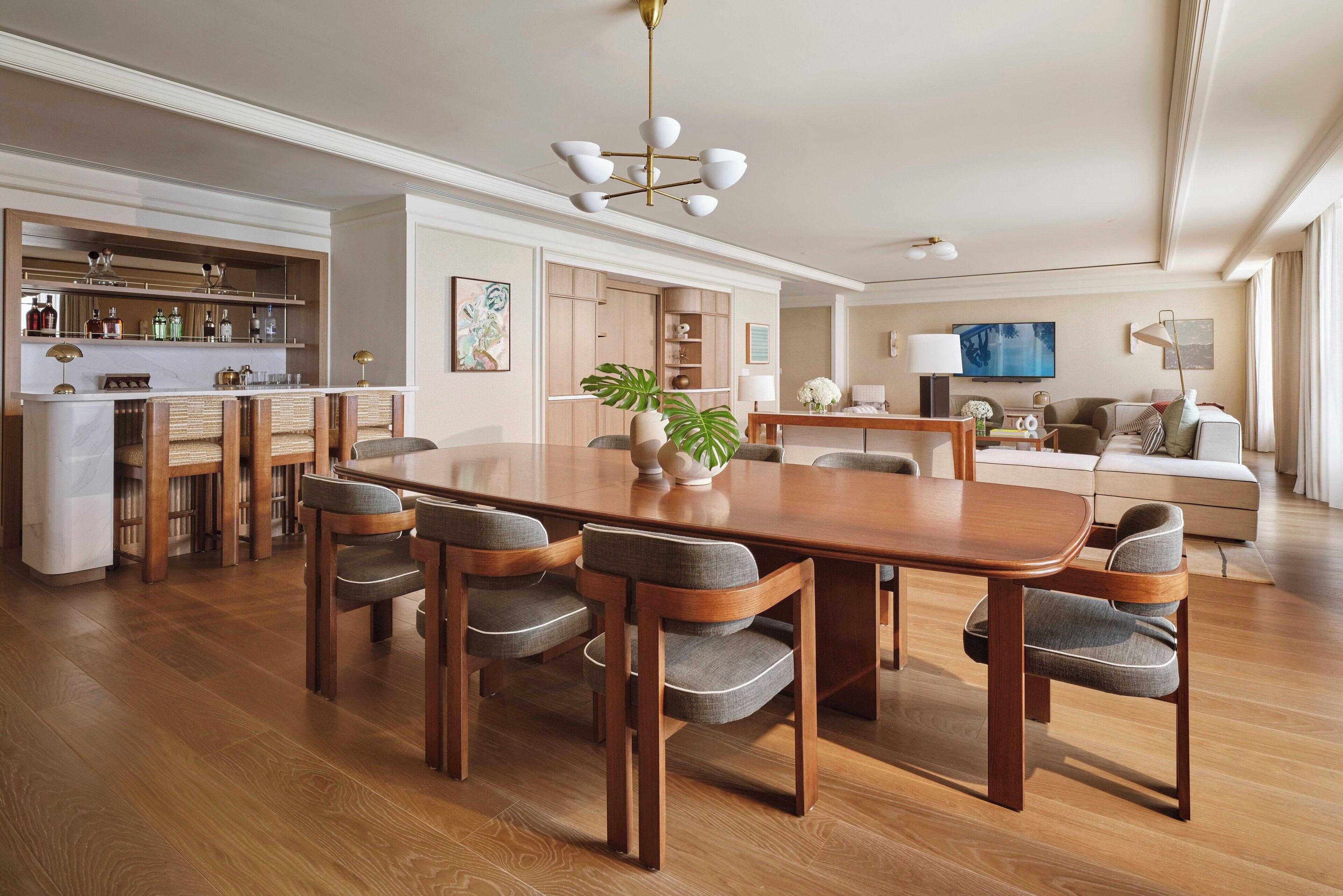 A spacious dining area with a wooden table and six chairs, a kitchen area with a bar, and a living room with a sofa and television.