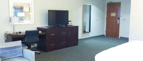 A hotel room with a bed, a desk with a chair, a television, a dresser, and a large mirror.