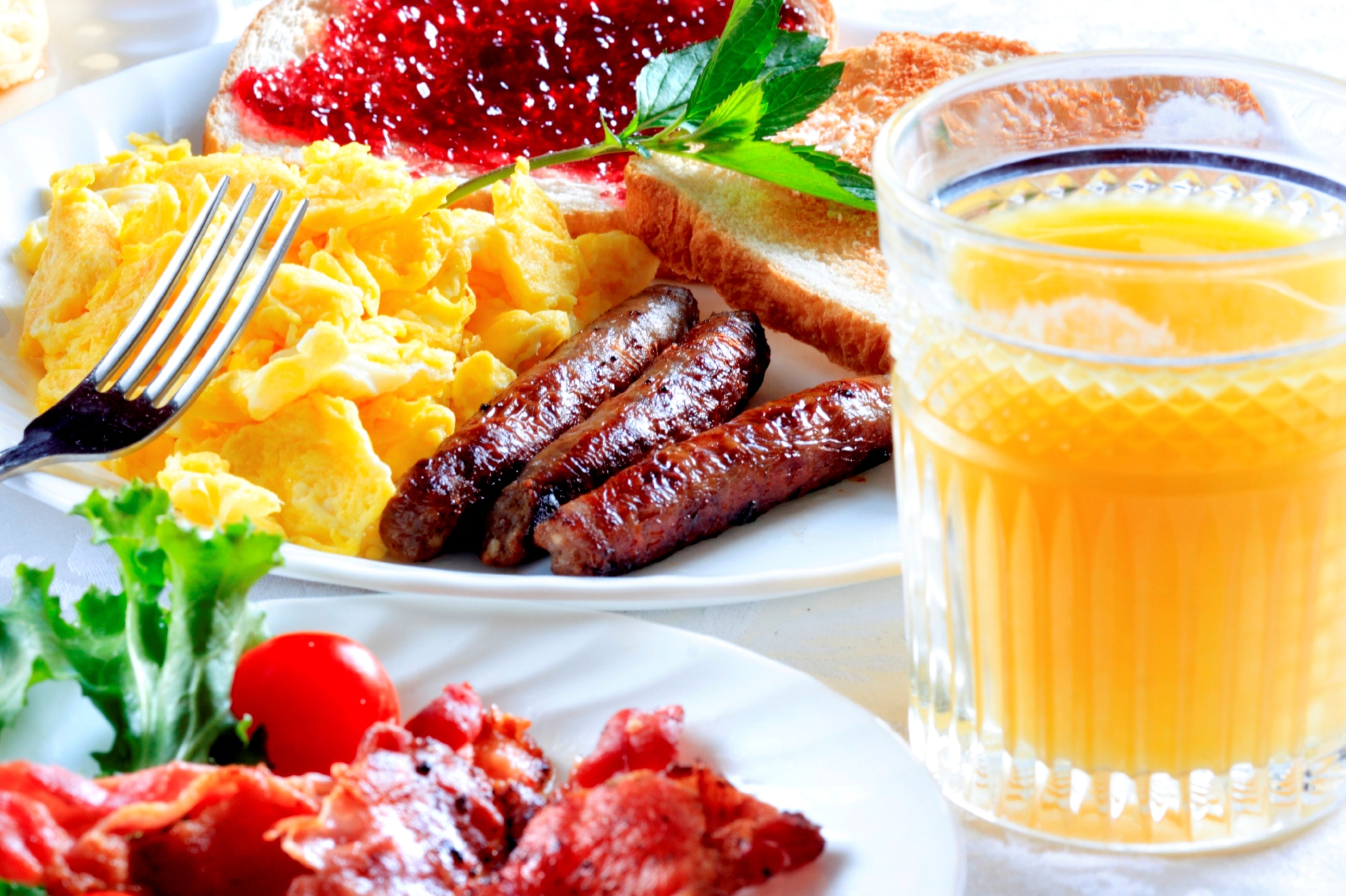 A breakfast plate with scrambled eggs, sausages, toast, jam, and a glass of orange juice.