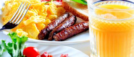 A breakfast plate with scrambled eggs, sausages, toast, jam, and a glass of orange juice.