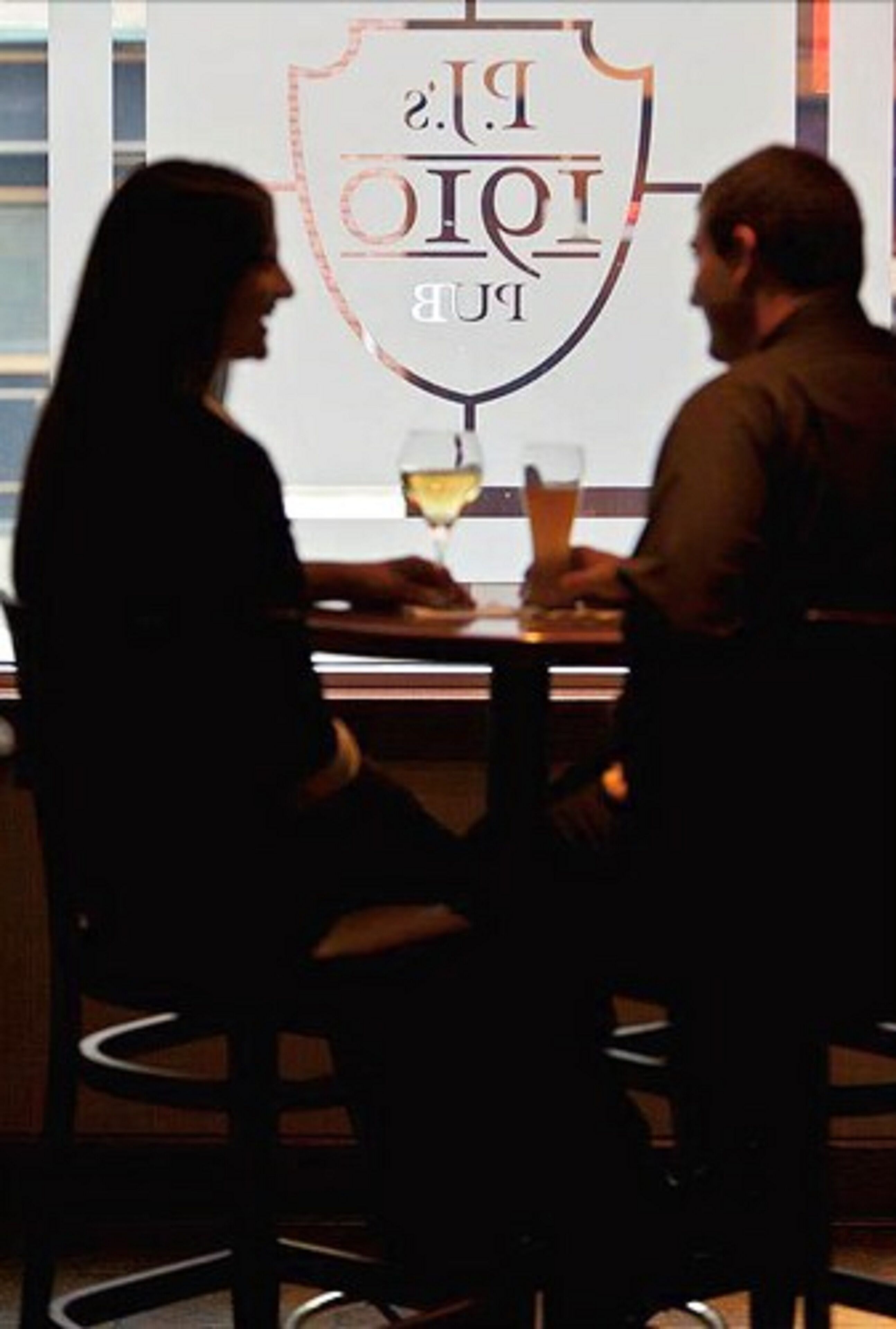 Deux personnes sont assises à une table dans un restaurant, et un logo est visible sur le mur derrière elles.