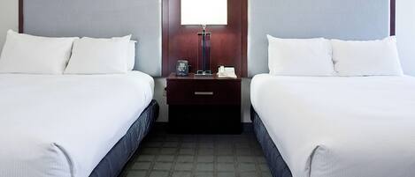 A hotel room with two beds, a nightstand with a lamp, and a telephone.