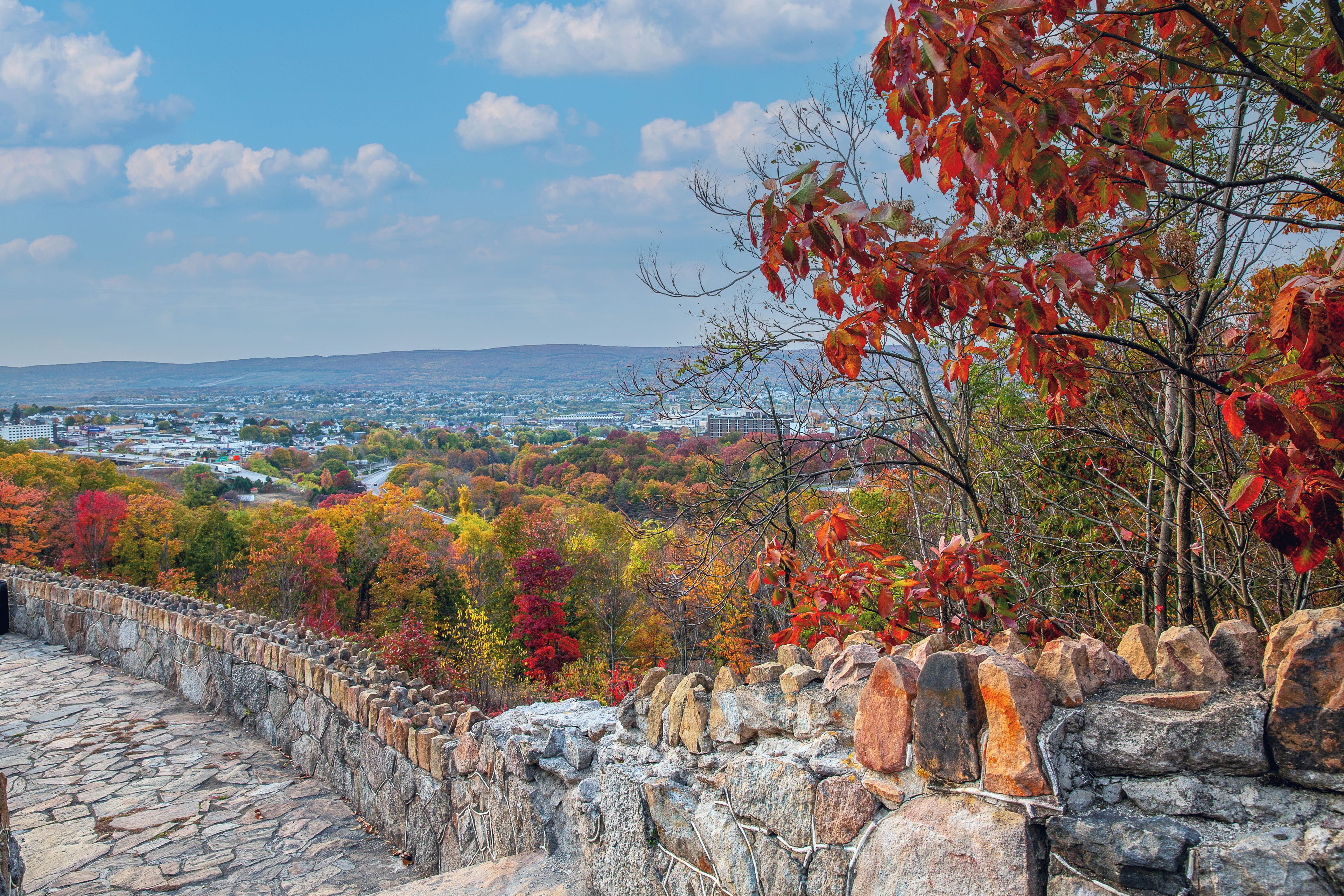 A stone wall with a view of a town and autumn foliage.