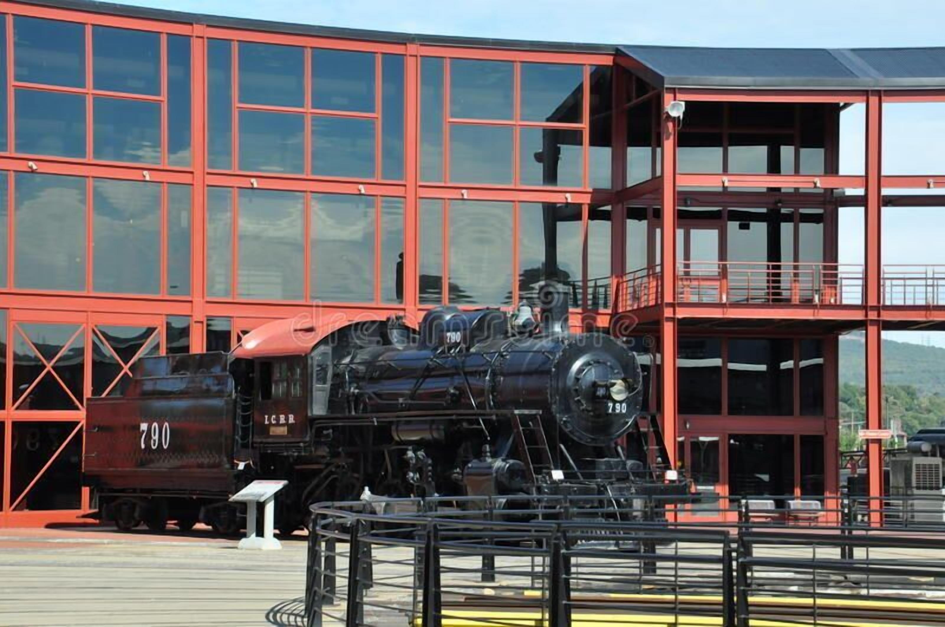 A black steam locomotive with the number 790, parked in front of a red building with large windows.