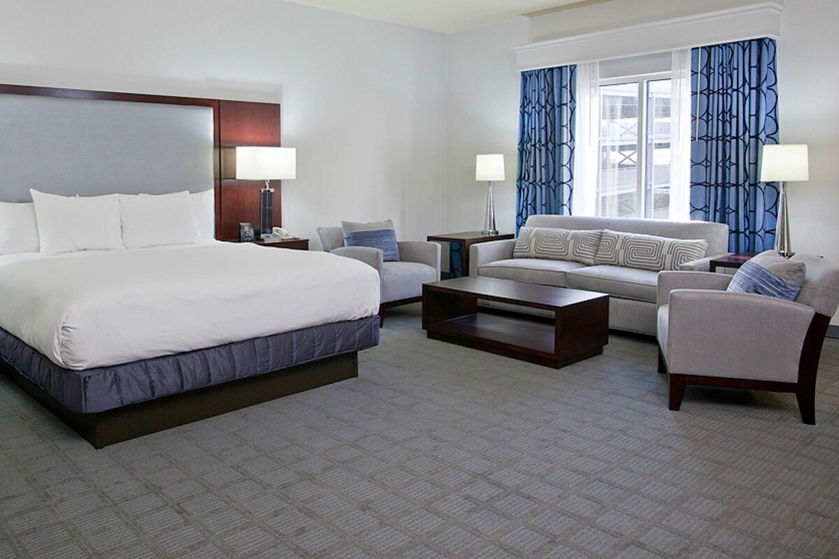 A hotel room with a large bed, a sofa, a coffee table, and two lamps.