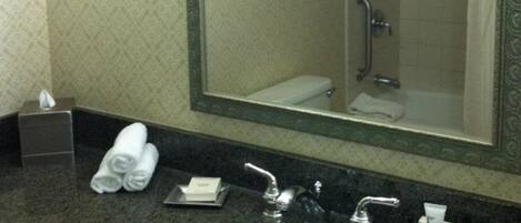 Un baño de hotel con un espejo grande, un lavabo, dispensador de toallas y una ducha.