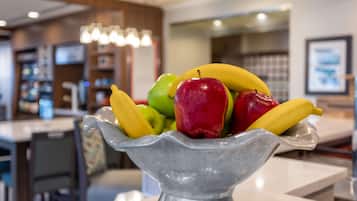 Un panier de fruits est posé sur une table dans un espace cuisine moderne, avec un bar et un comptoir en arrière-plan.