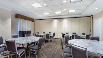 Een vergaderzaal met ronde tafels, stoelen en een vloerbedekking.