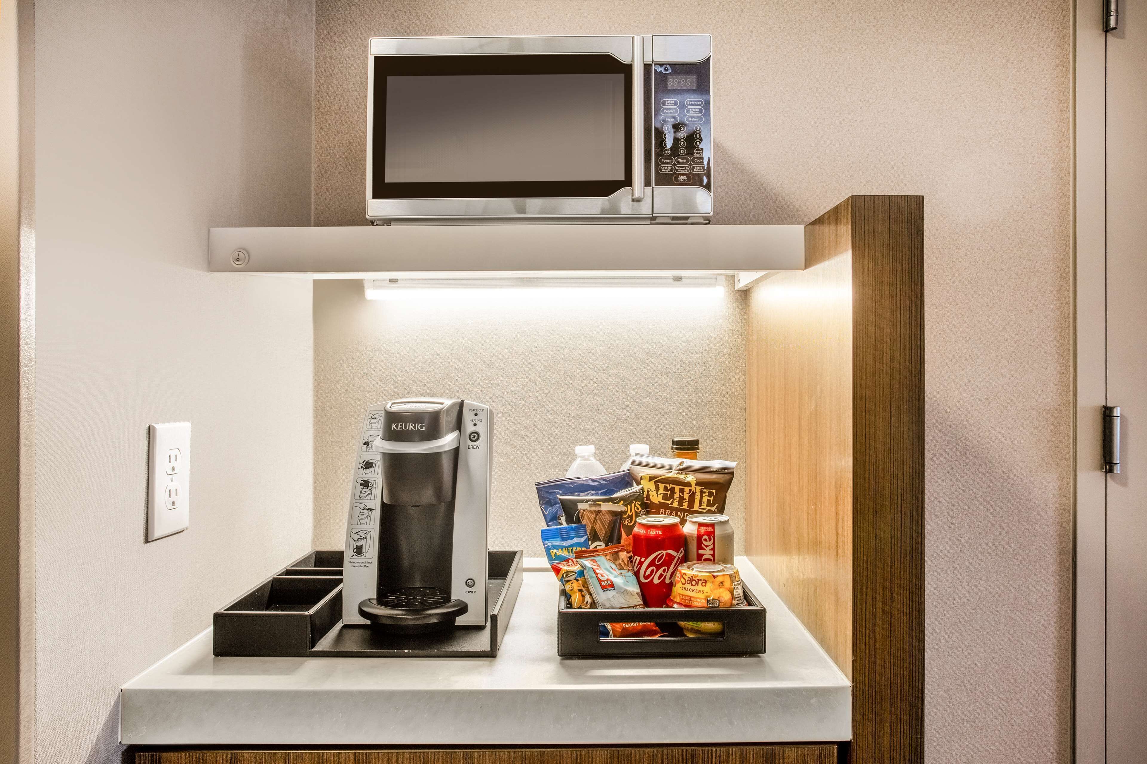 Een kitchenette met een koffiezetapparaat, magnetron en een schotel met snacks.